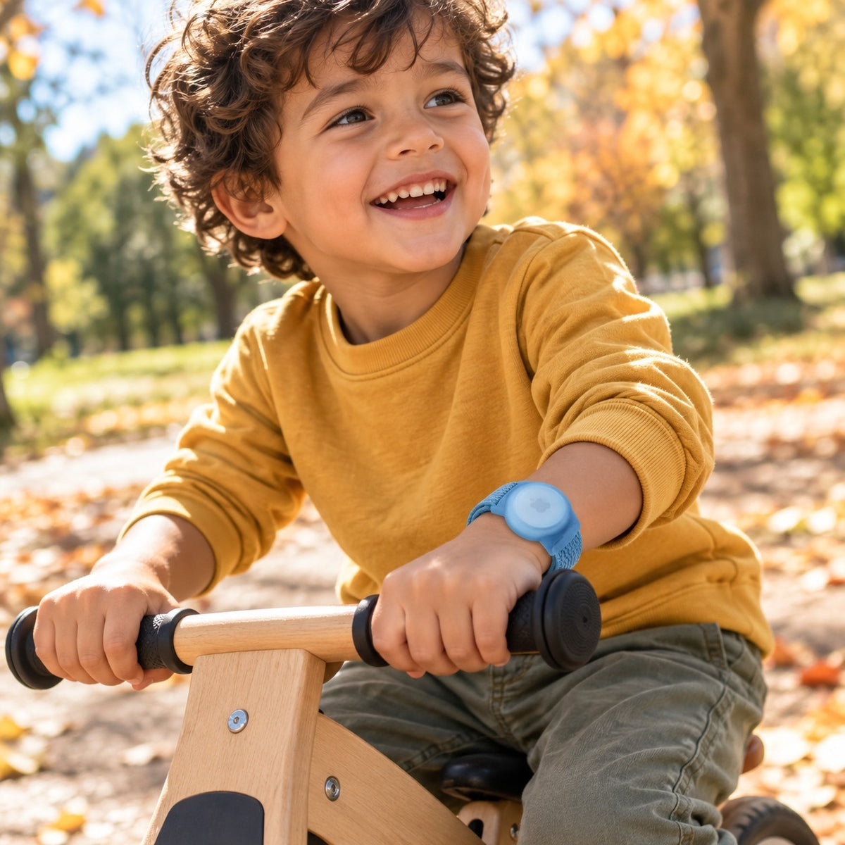 Junge auf dem Laufrad im Park, blaues AirTag-Kinderarmband am Handgelenk