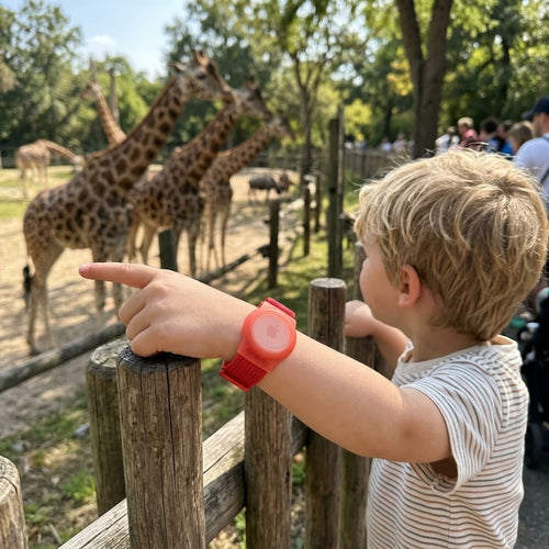 Kind im Zoo zeigt auf Giraffen, rotes AirTag-Kinderarmband am Handgelenk