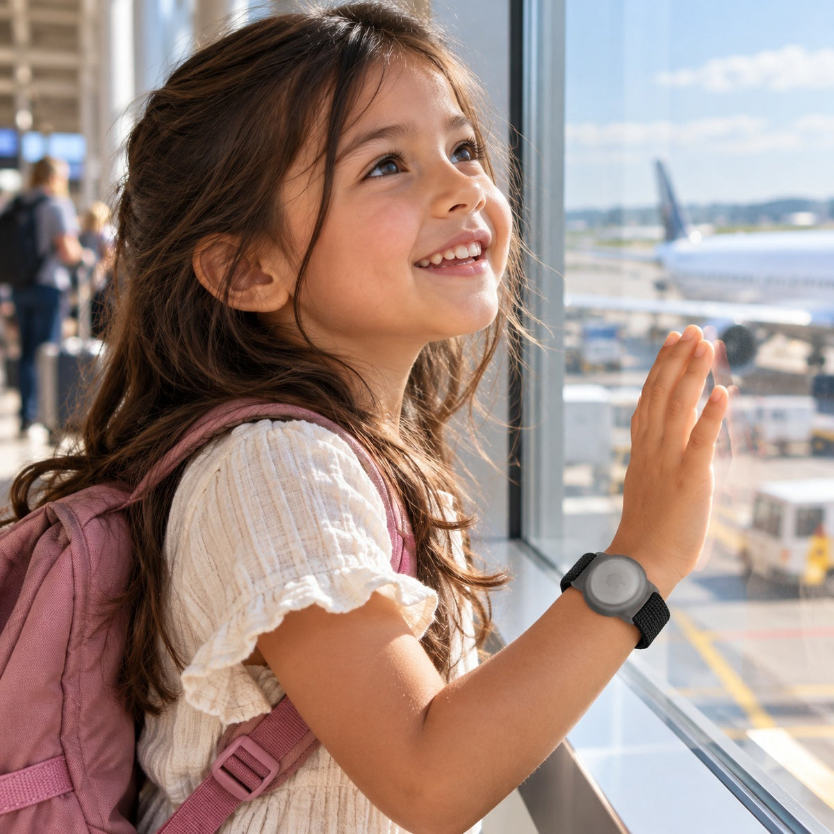 Mädchen am Flughafenfenster, schwarzes AirTag-Kinderarmband am Handgelenk